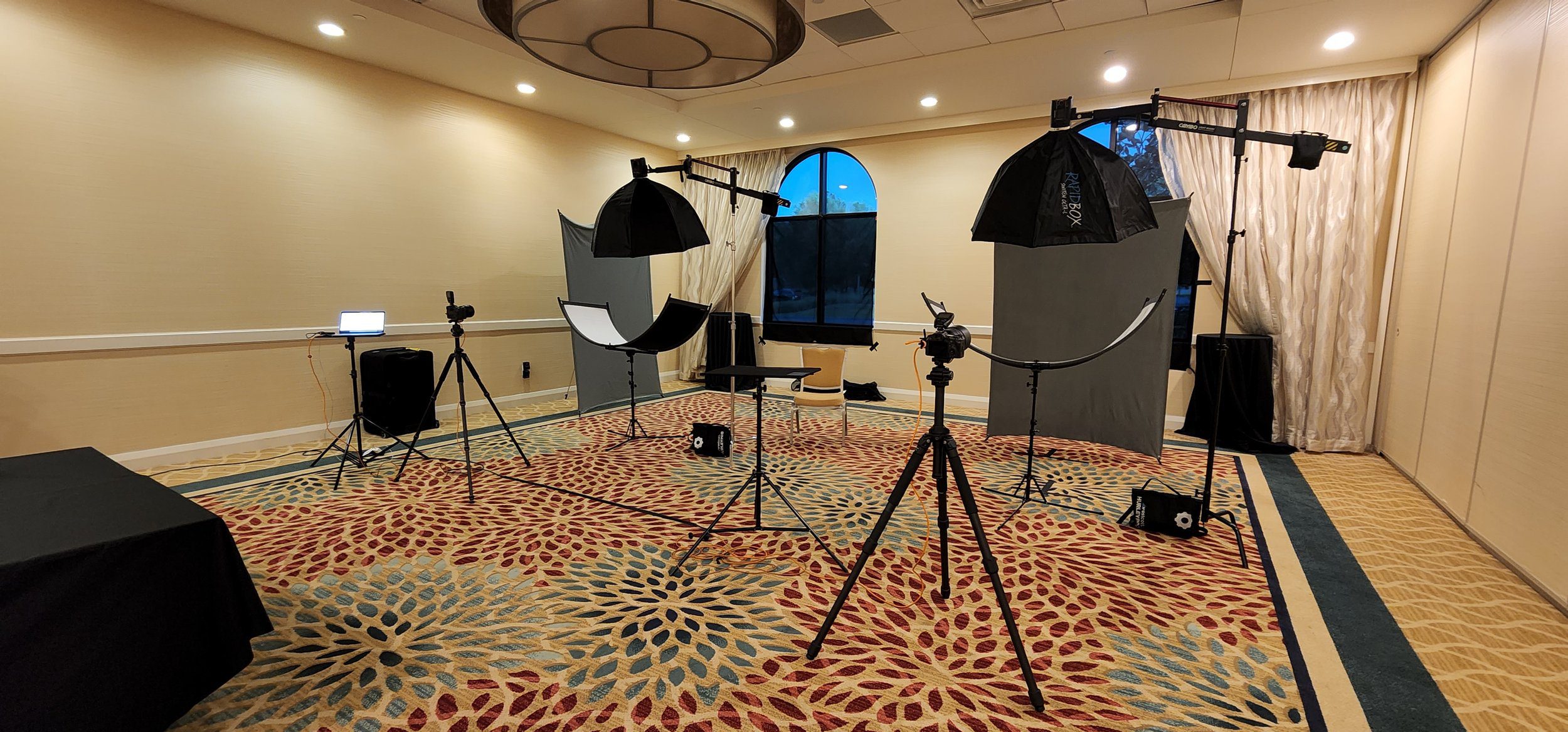 Behind the scenes of an on-location team headshot setup with studio lights, cameras, and gray backdrops inside a conference room